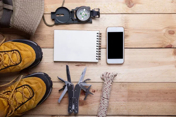 Equipo de planificación de emergencias: brújula, multiherramienta, cuerda, cuaderno y móvil sobre mesa de madera
