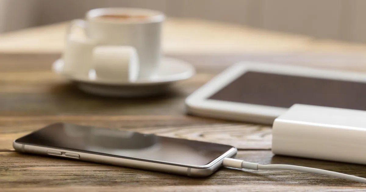 Power bank portatil cargando un movil sobre mesa de madera, energia de respaldo para emergencias